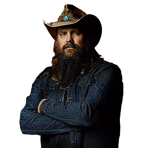 A bearded man wearing a cowboy hat with a turquoise accent and a denim jacket, standing with his arms crossed.