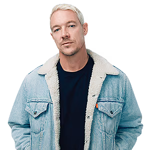 A man with short blonde hair wears a black shirt under a light-wash denim jacket with a white sherpa lining.